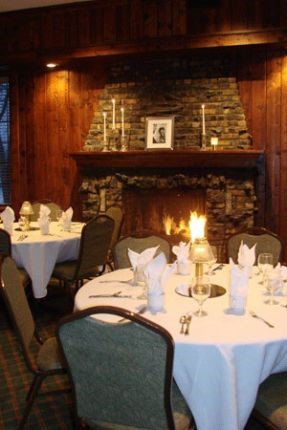 The room features a cozy fireplace, rich wood paneled walls, pub bar, and large windows on two sides.